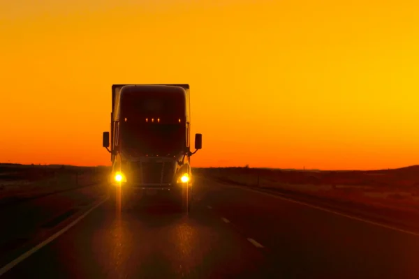 Front of semi truck alone on the road at dusk with headlights on