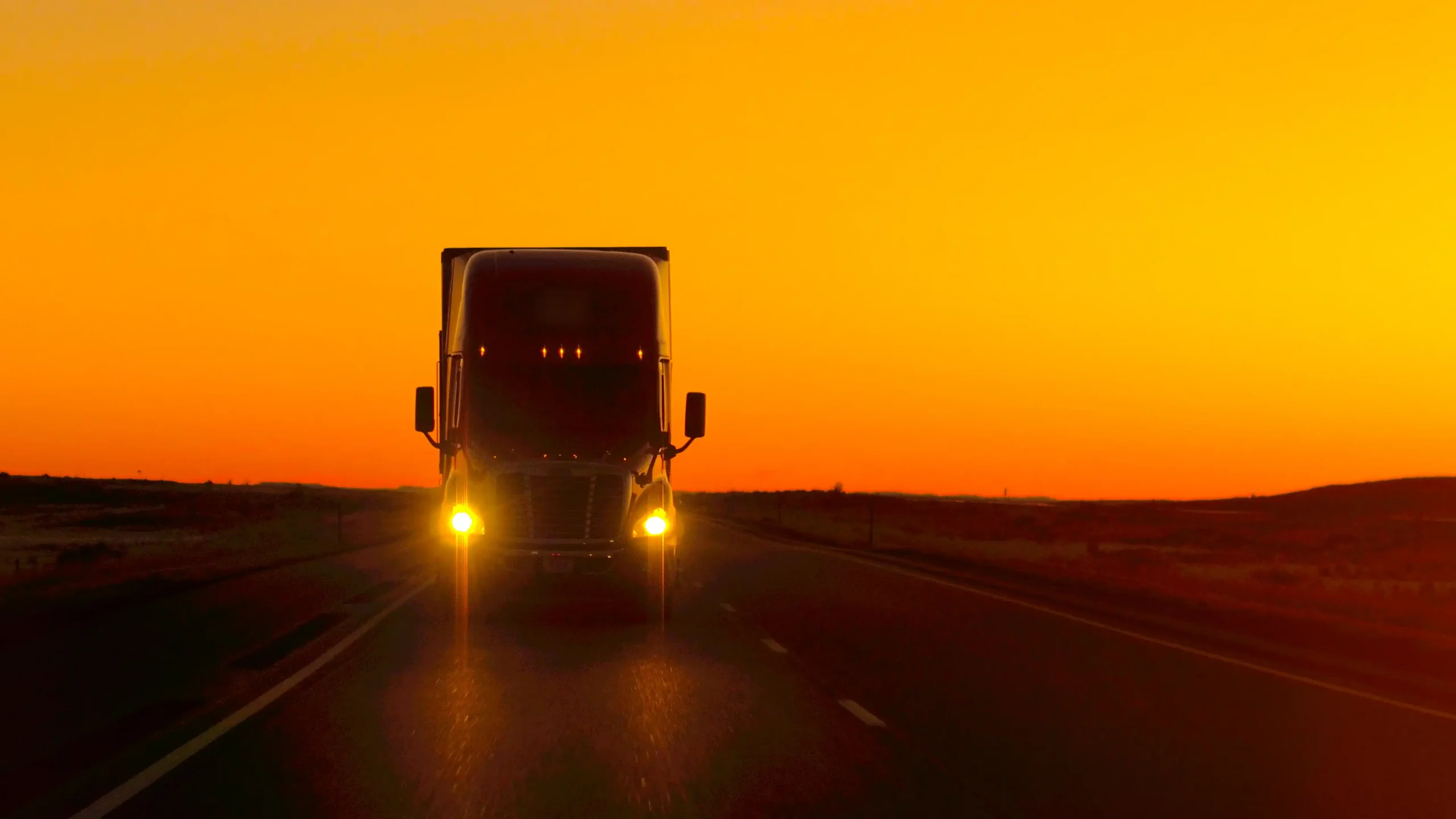 Front of semi truck alone on the road at dusk with headlights on