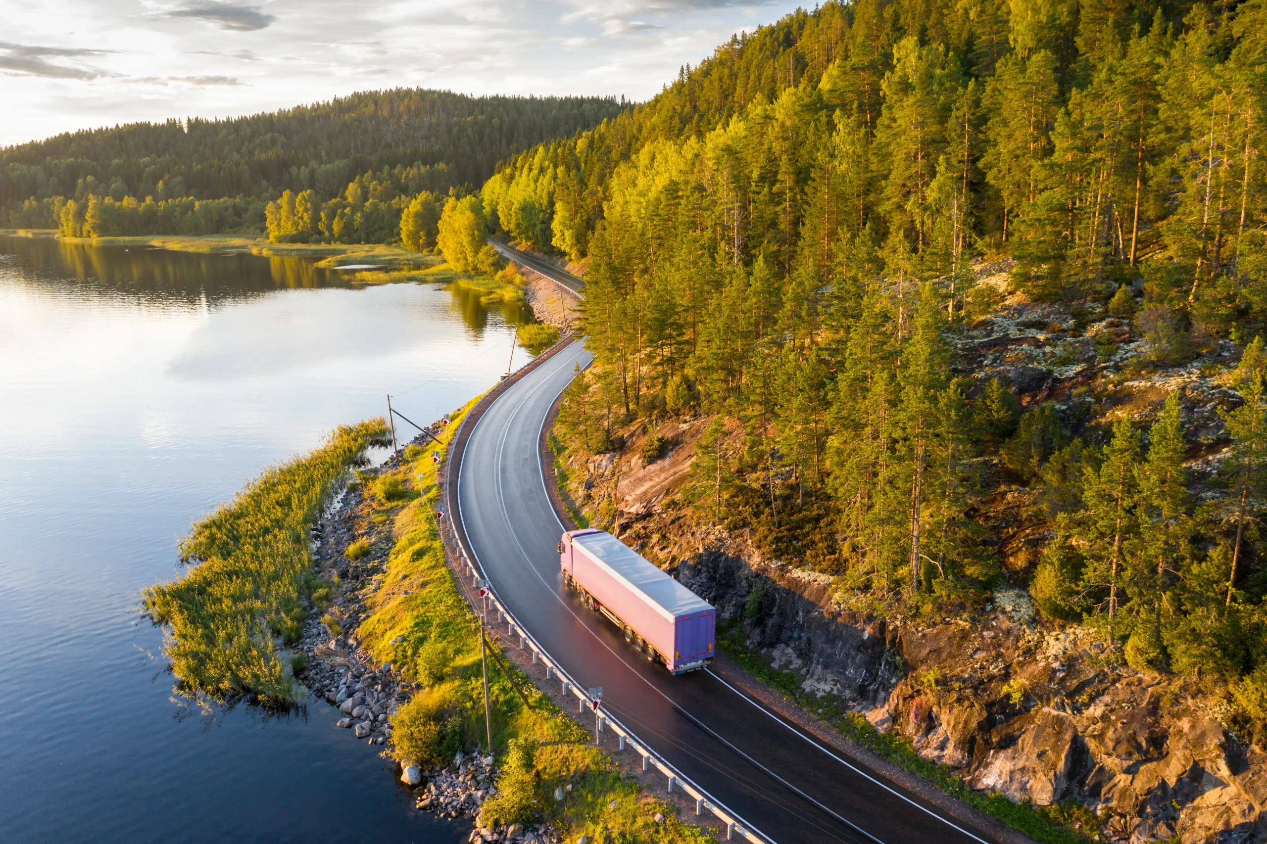 semi truck on two lane road going around a bend with lake and mountain