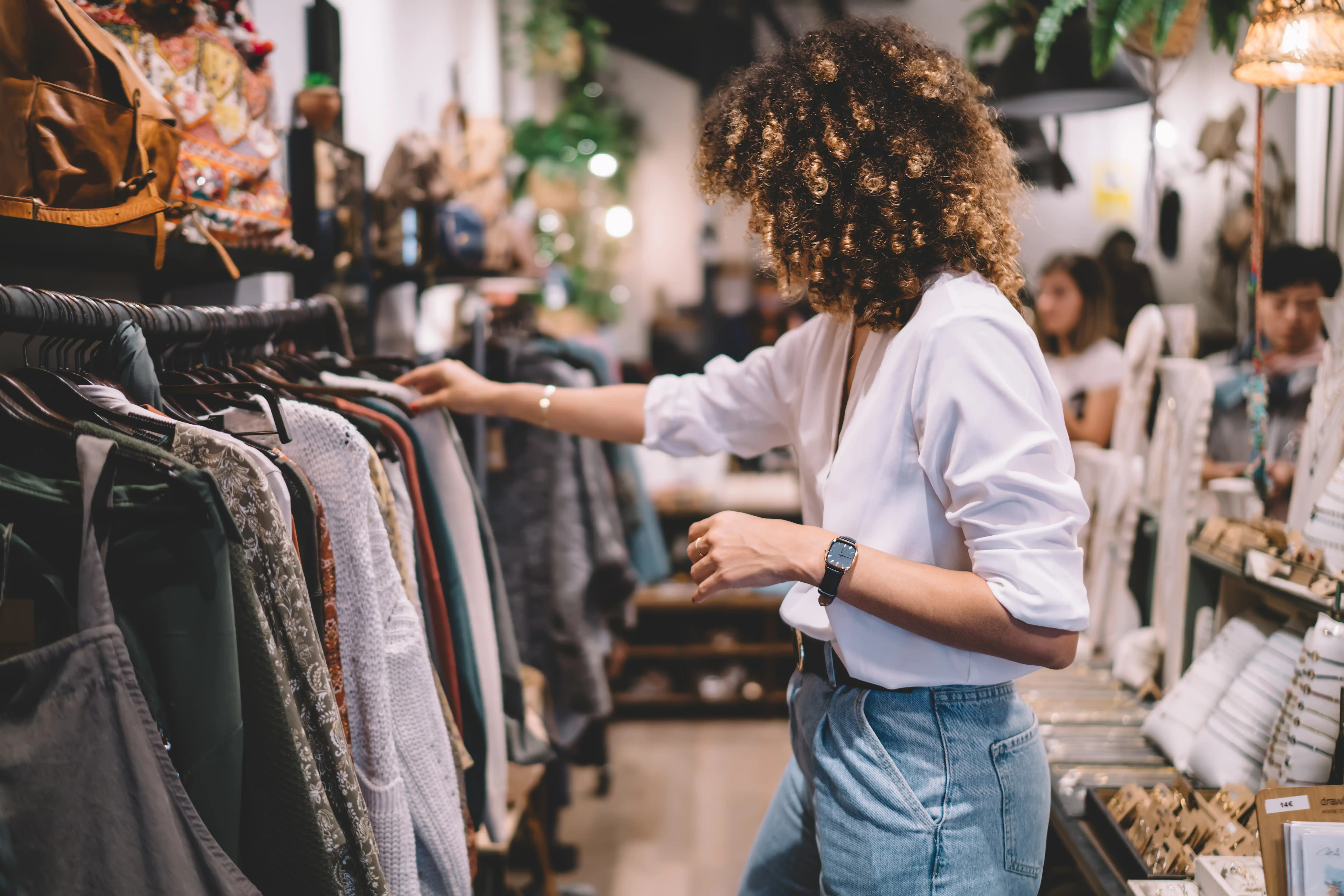 woman in jeans and white top looking at a shirt on the rack at a clothing store