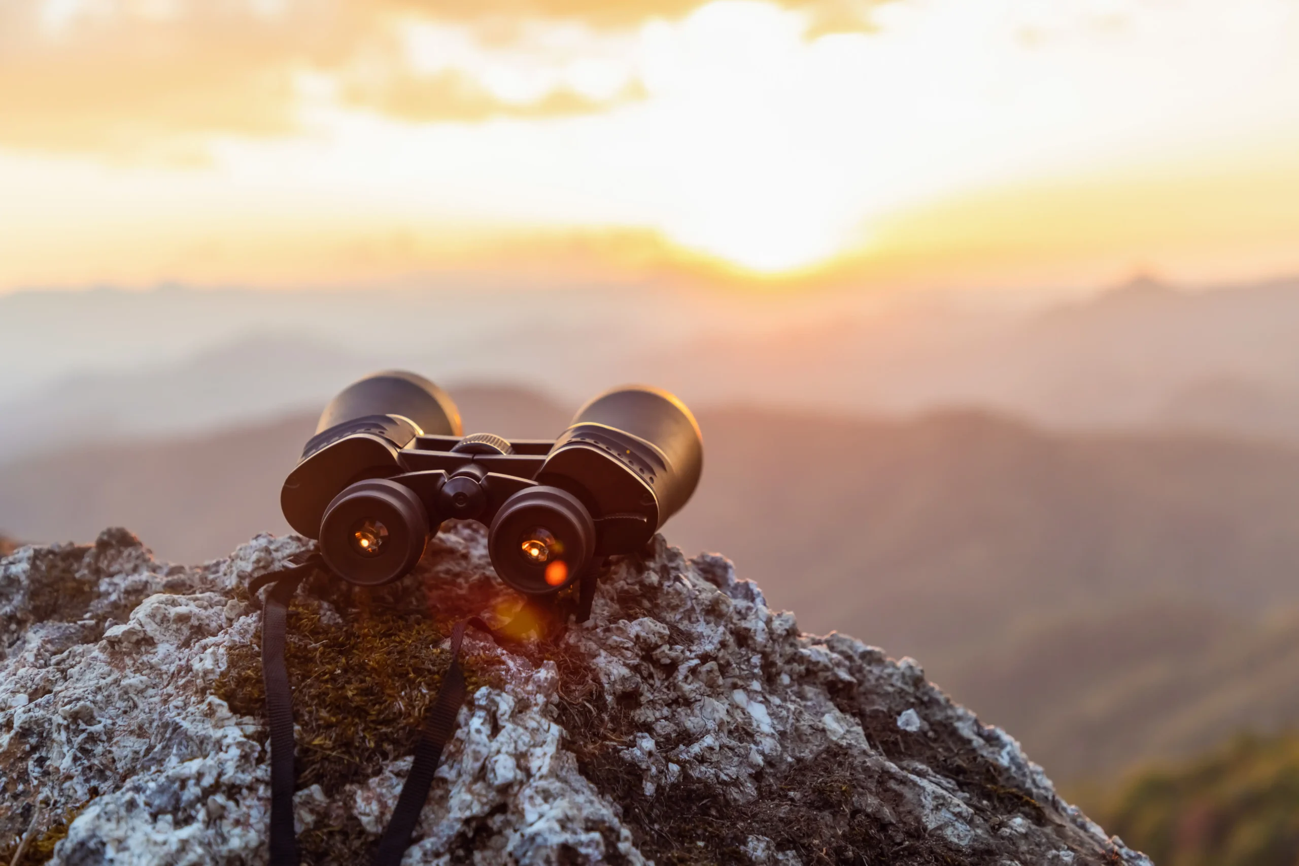 A pair of binoculars resting at the top of a mountain looking into the distant sky