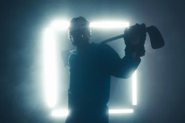 Backlit hockey player holding stick across shoulders