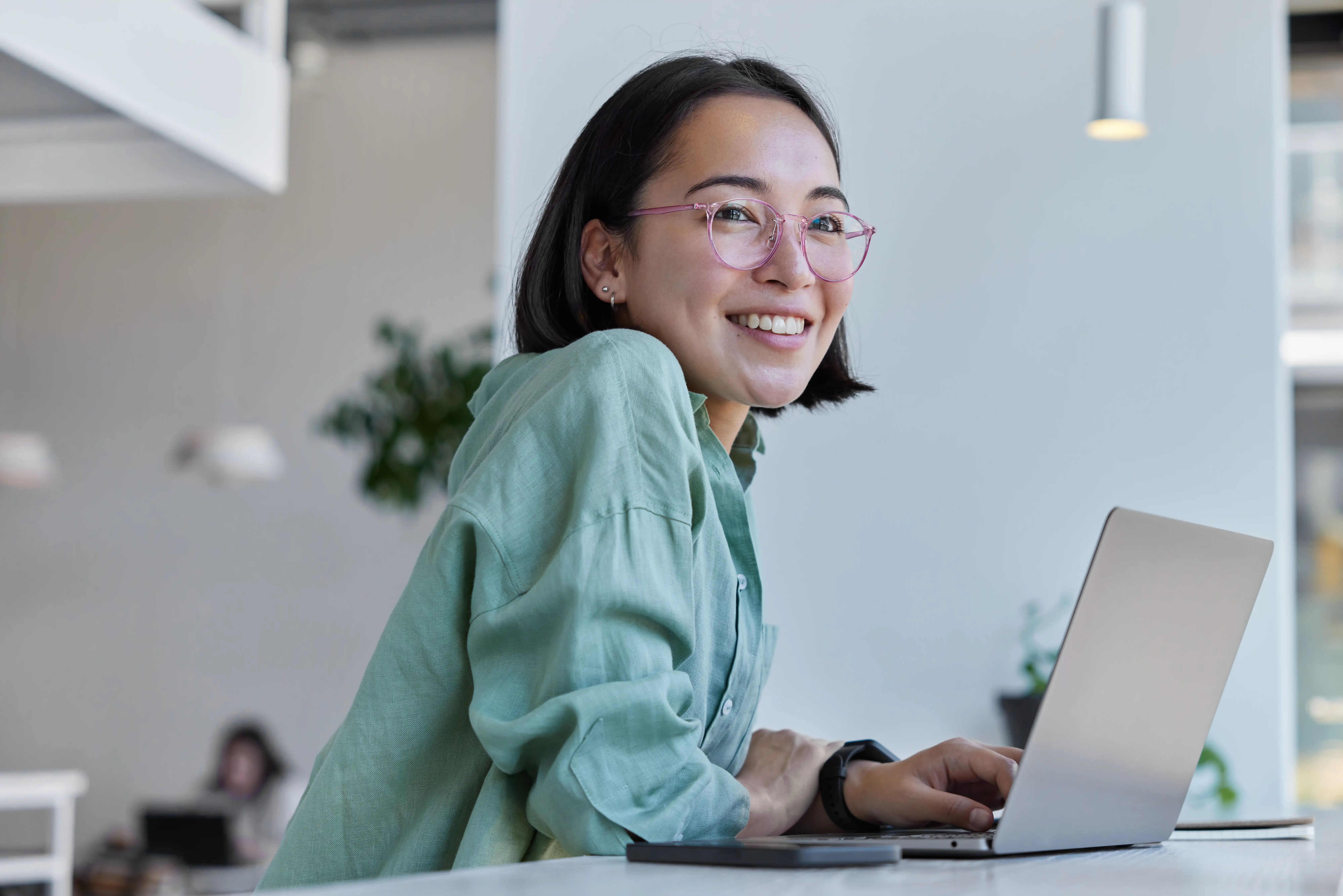 Woman at desk smiling wearing mint shirt and pink glasses