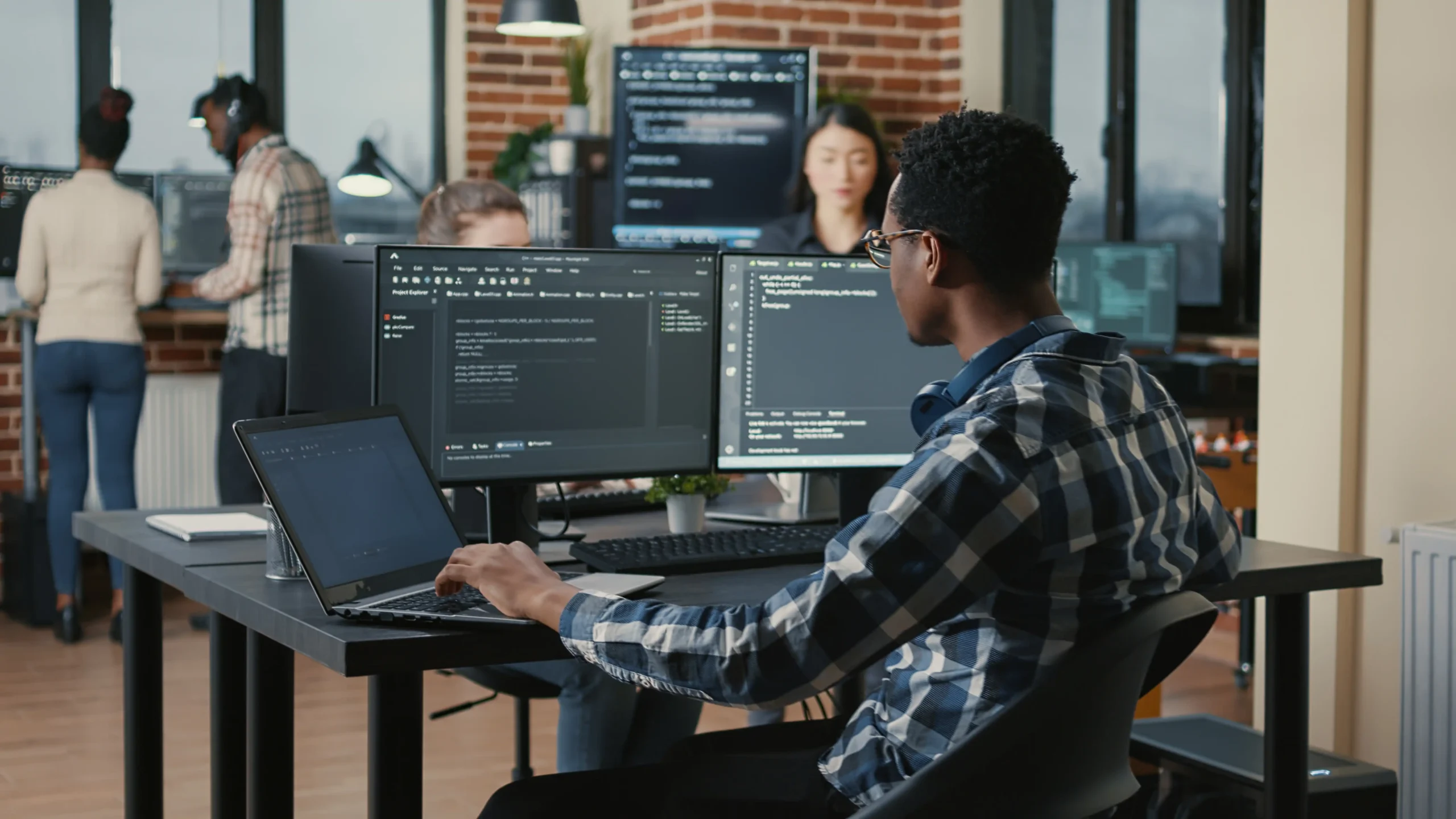 Man at office desk with multiple monitors working on coding