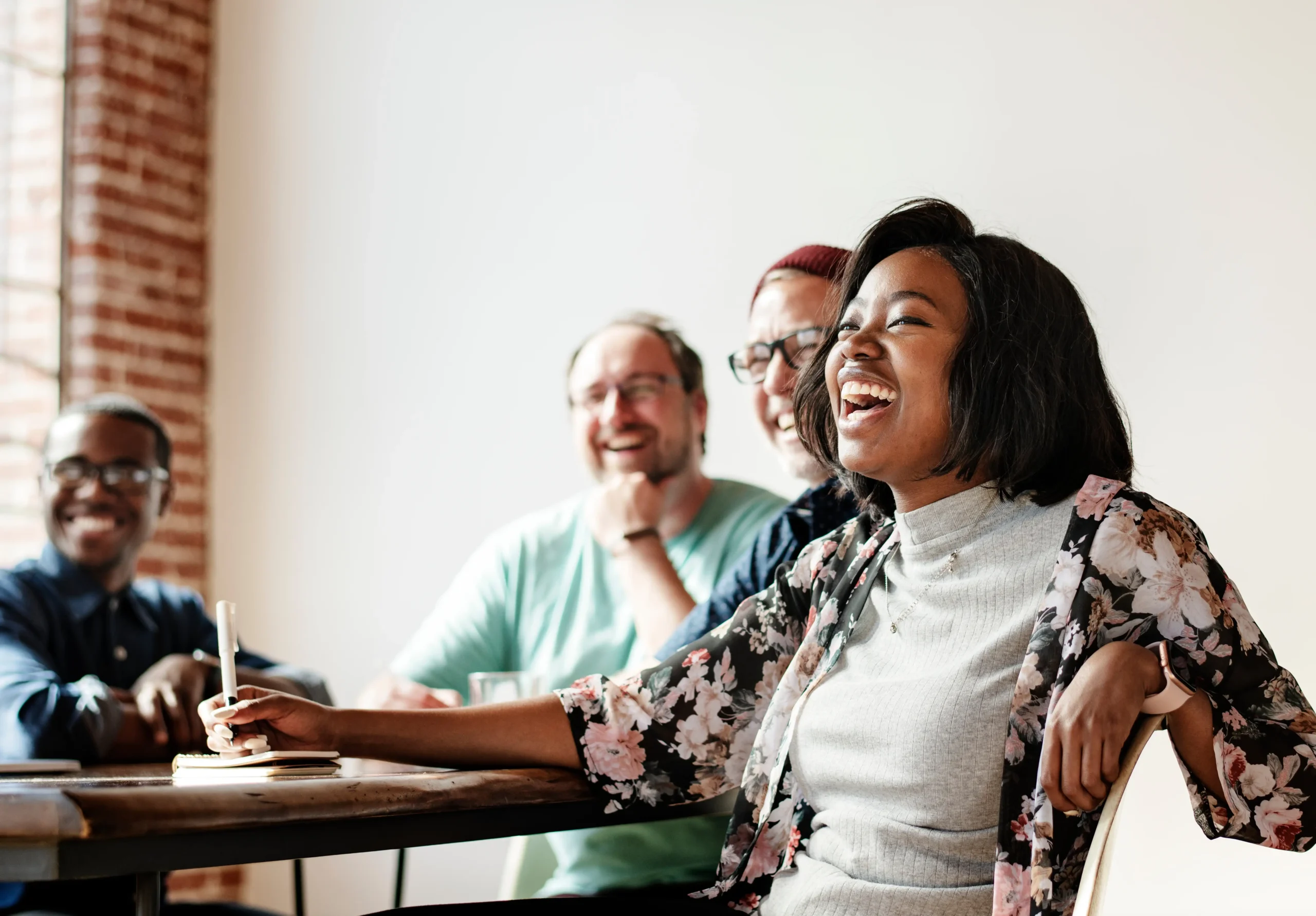 Four coworkers sitting at a conference table laughing while they take notes