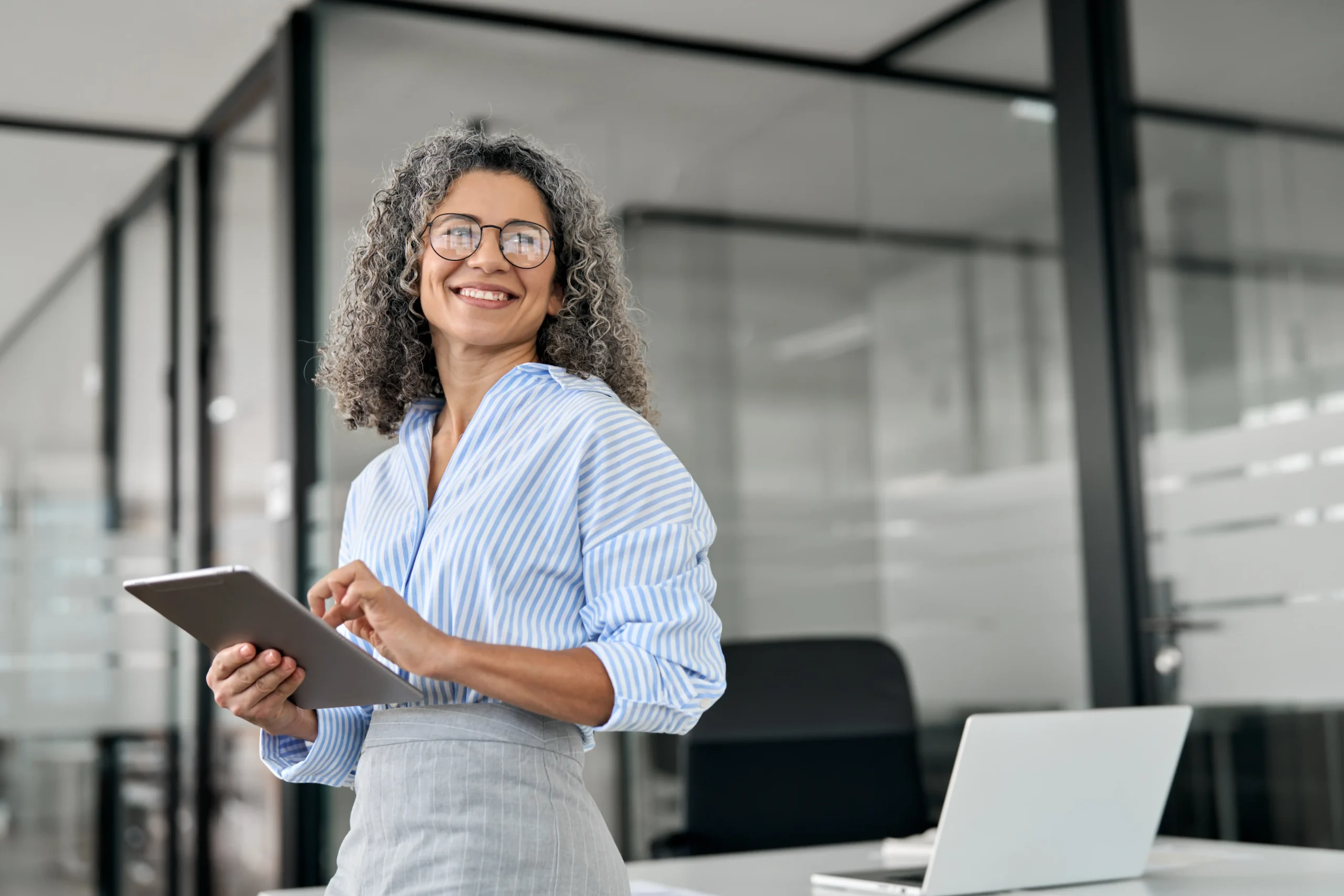 Woman leaning on office desk with ipad smiling