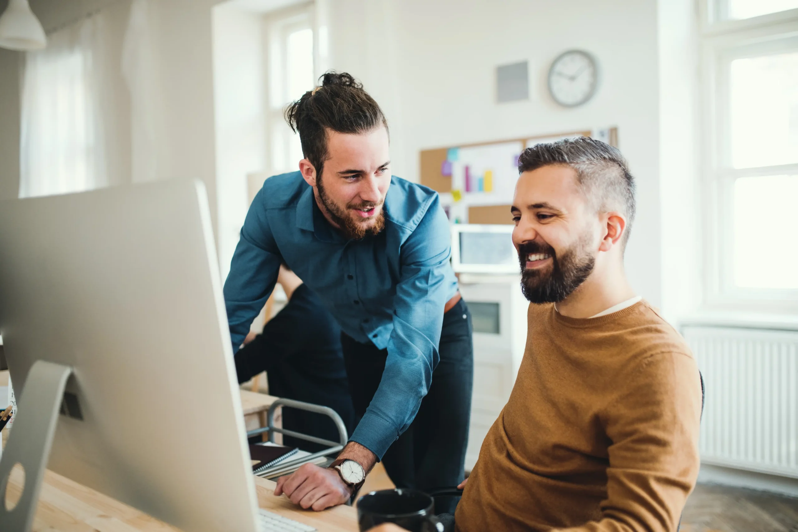 Two colleagues at a large desk with monitor solving a problem together