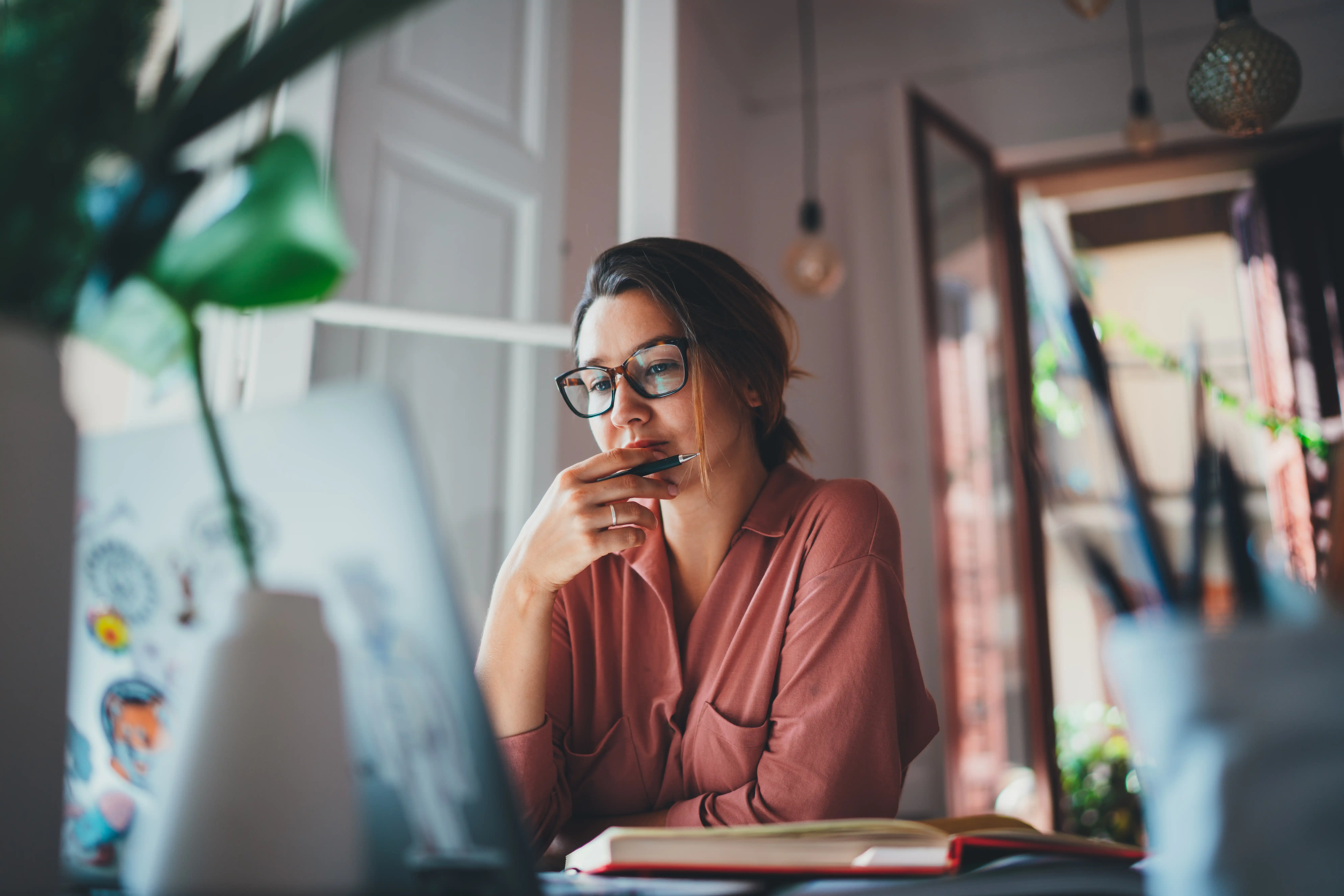 Thoughtful lady in glasses with pen at desk