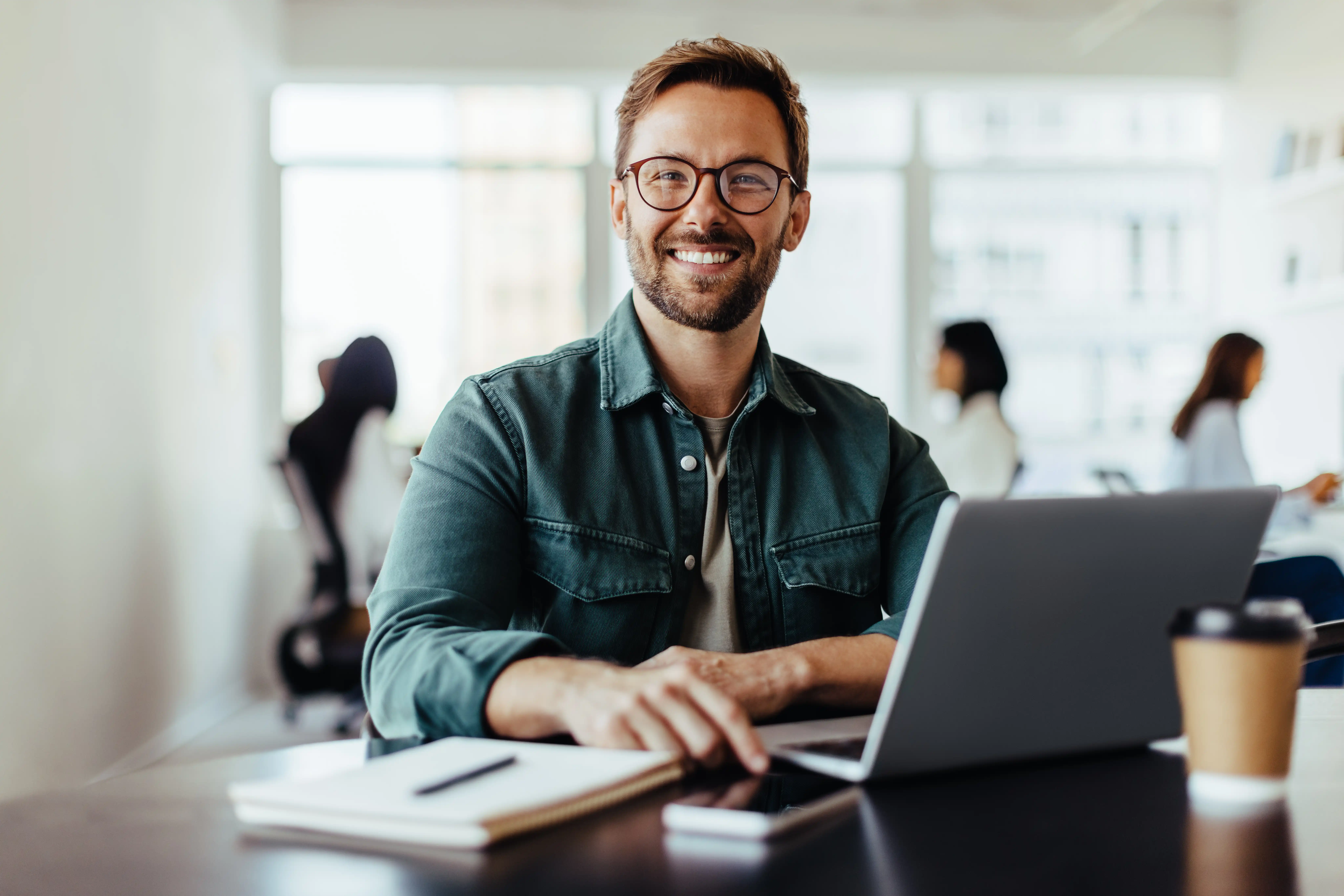 man smiling at camera with coffee at desk