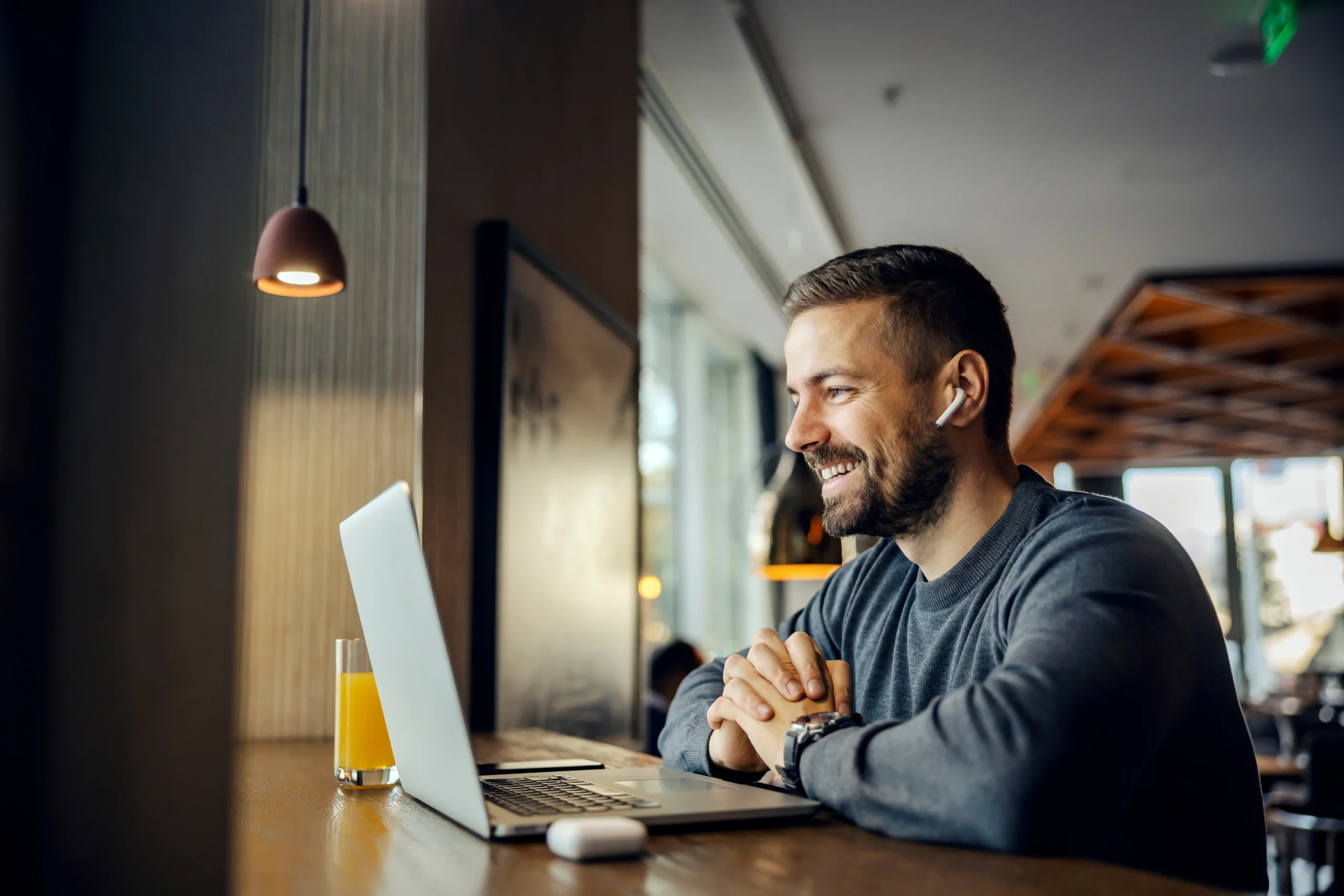 man wearing ear buds on laptop with orange juice