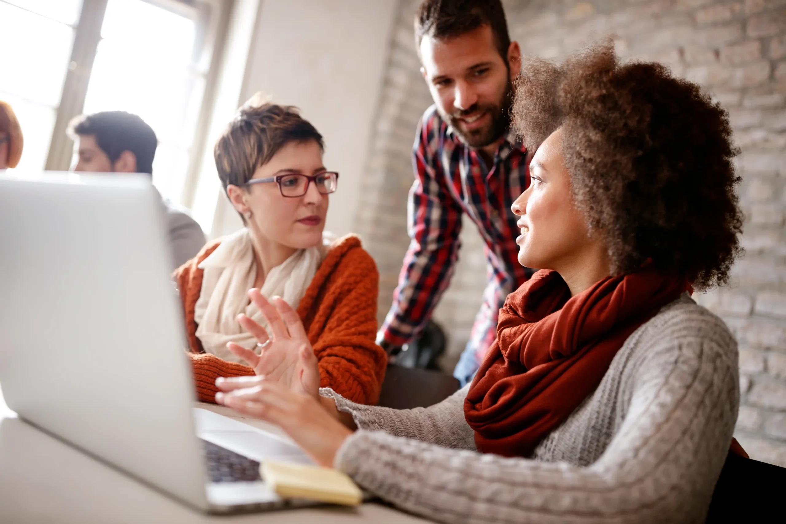 Three coworkers in a shared office collaborating at a laptop
